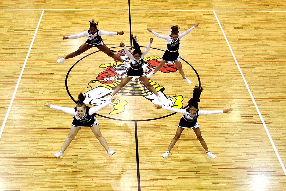 A high school cheer squad doing a jump in formation on a basketball court