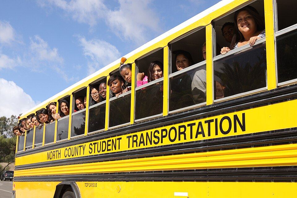 Students smiling out of the windows of a yellow school bus